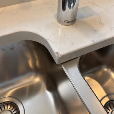 Stone worktop corner beside a kitchen sink before repair, with a visible chip