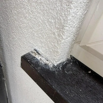Before: chipped and scuffed black uPVC trim at the corner of a textured wall